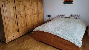 A bedroom with a wooden wardrobe, a bed with a patterned bedspread, a nightstand with a lamp, and a framed cityscape painting on the wall. - Vacation apartment with garden in Drochtersen (Drochtersen)