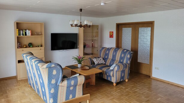 A living room with a sofa, armchair, and a TV mounted on the wall. - Vacation apartment with garden in Drochtersen (Drochtersen)