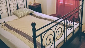 A bed with a metal frame, a bedside table with a lamp, and a window with red curtains.