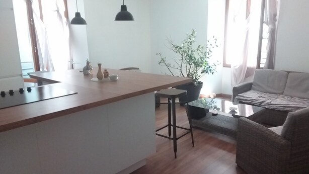 A modern kitchen with a central island, bar stools, a dining table, and a sofa.