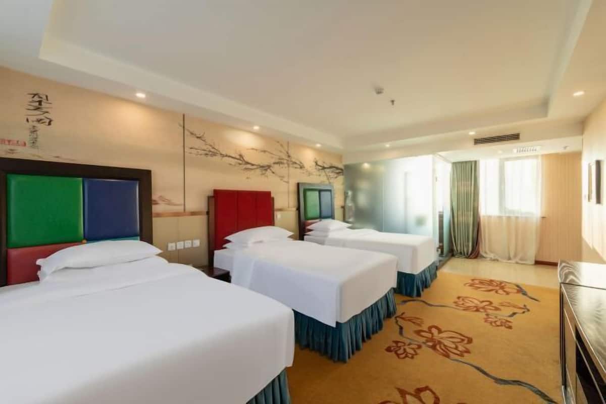 A hotel room with three beds, a large window with curtains, and a floral carpet.