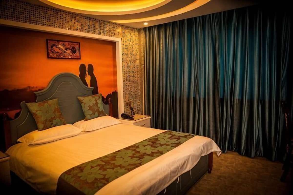 A hotel room with a large bed, a nightstand, a wall-mounted clock, and a curtain.
