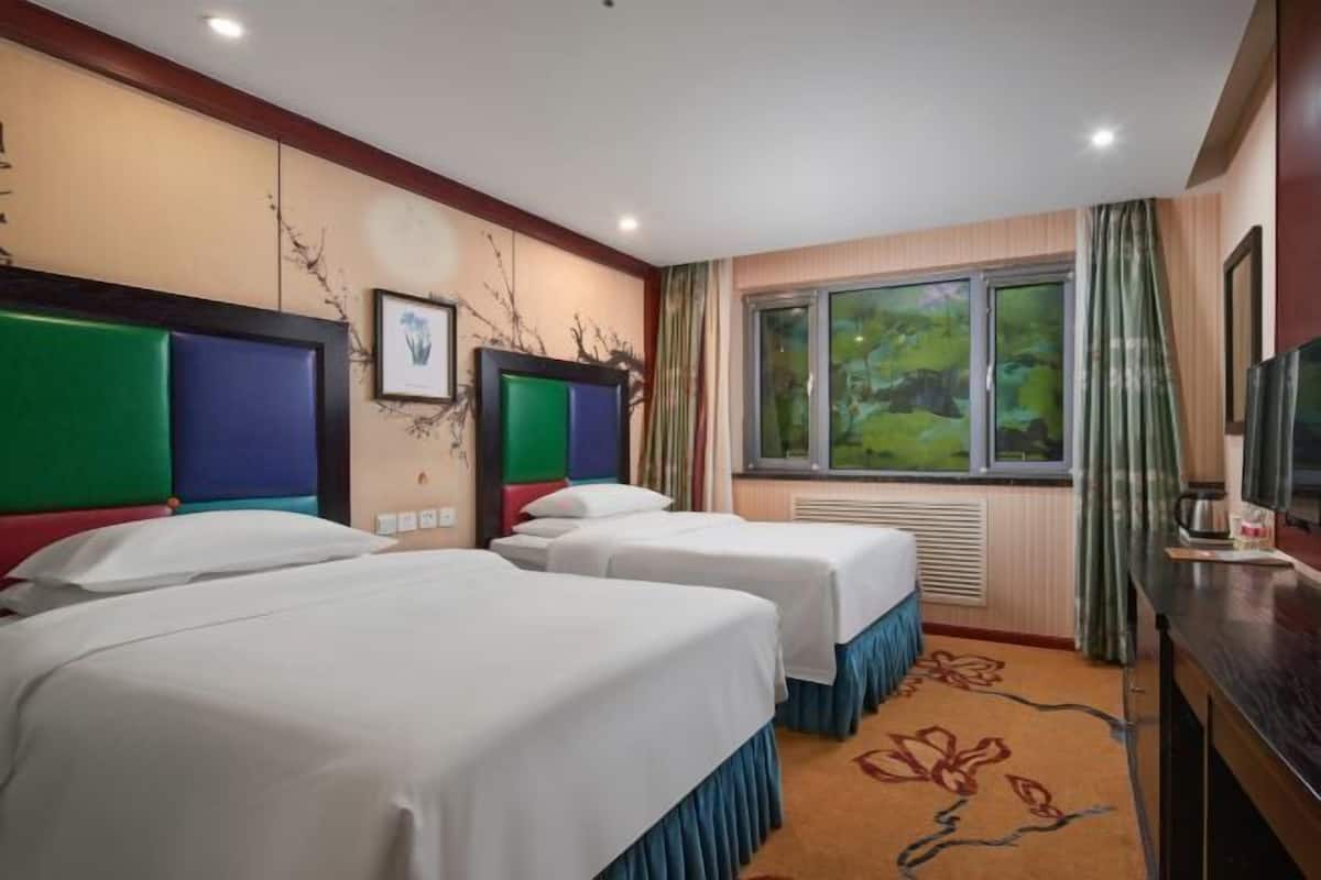 A hotel room with two beds, a large window with a view, and a television on the right side.