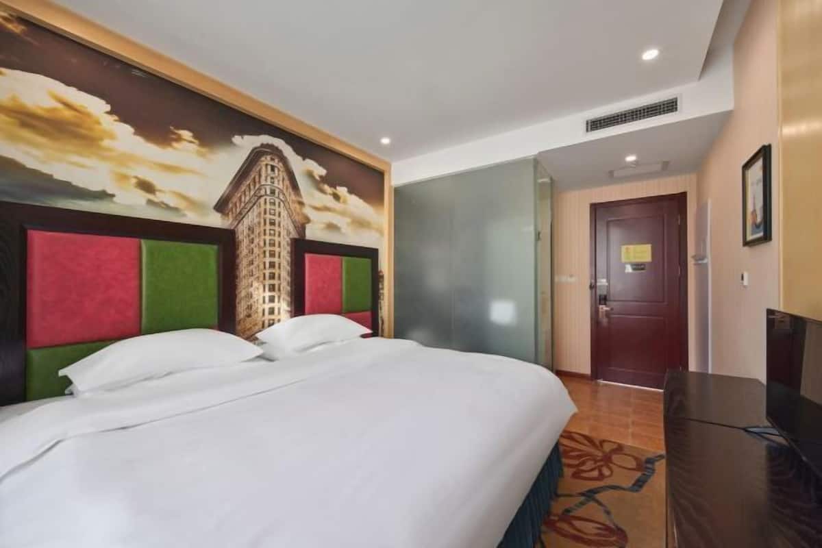 A hotel room with a bed, a television, a door, and a wall with a cityscape mural.