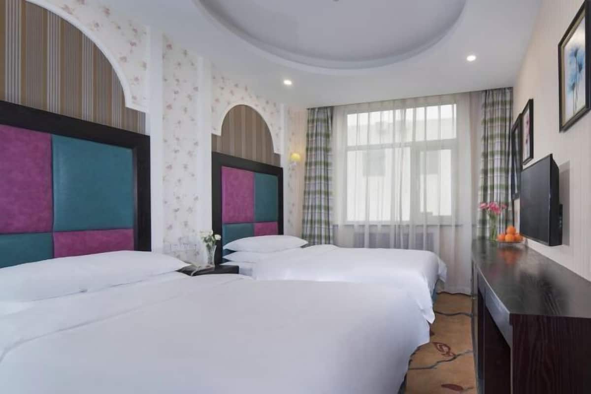 A hotel room with two beds, a desk, a TV, and a window with curtains.