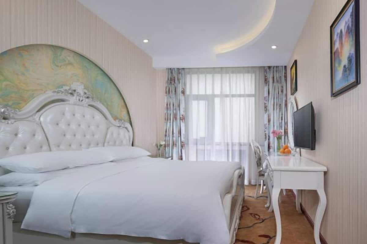 A hotel room with a large bed, a desk, a television, and a large painting on the wall.