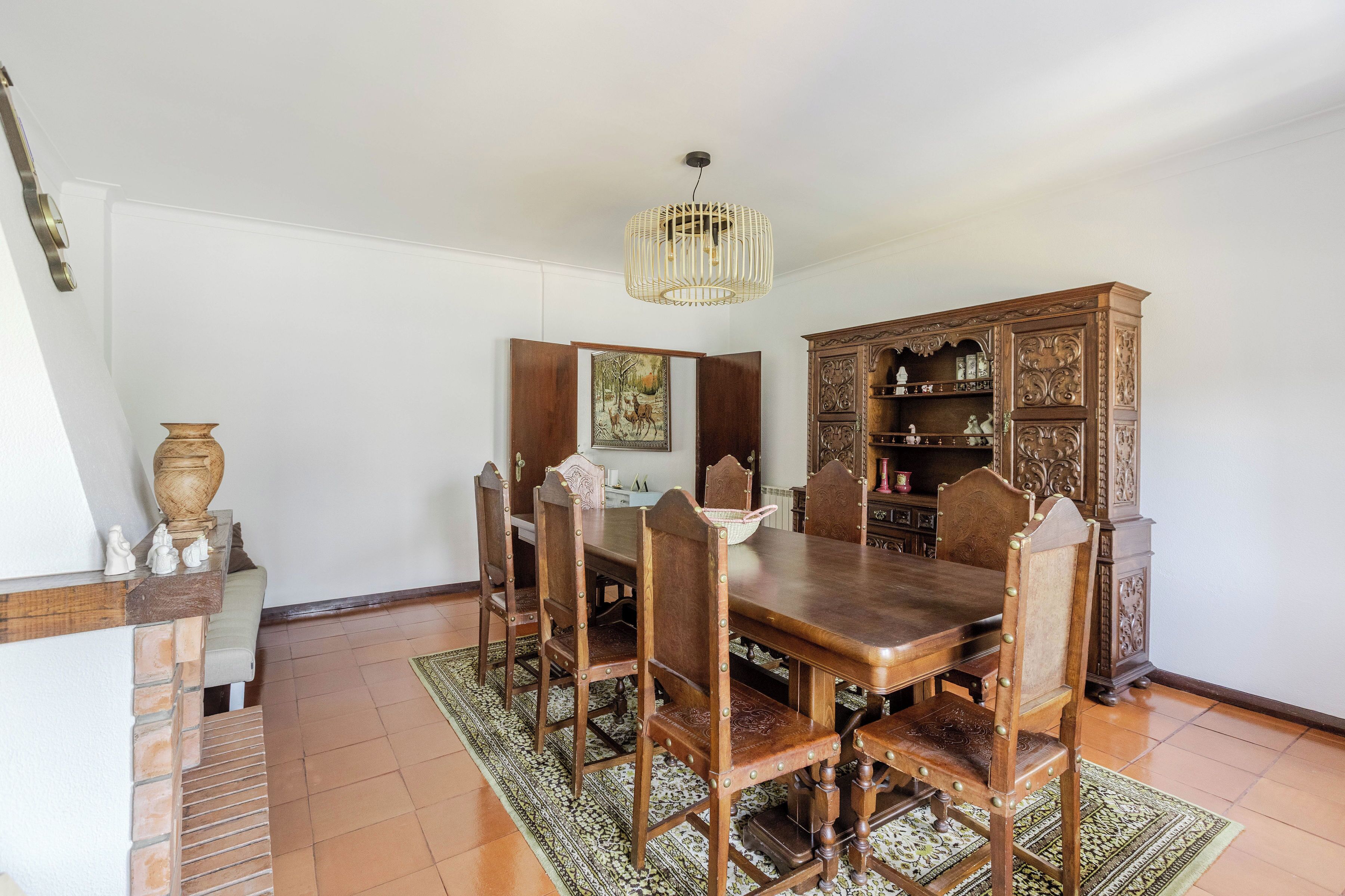 A dining room with a wooden table and chairs, a chandelier, and a cabinet with decorative carvings.