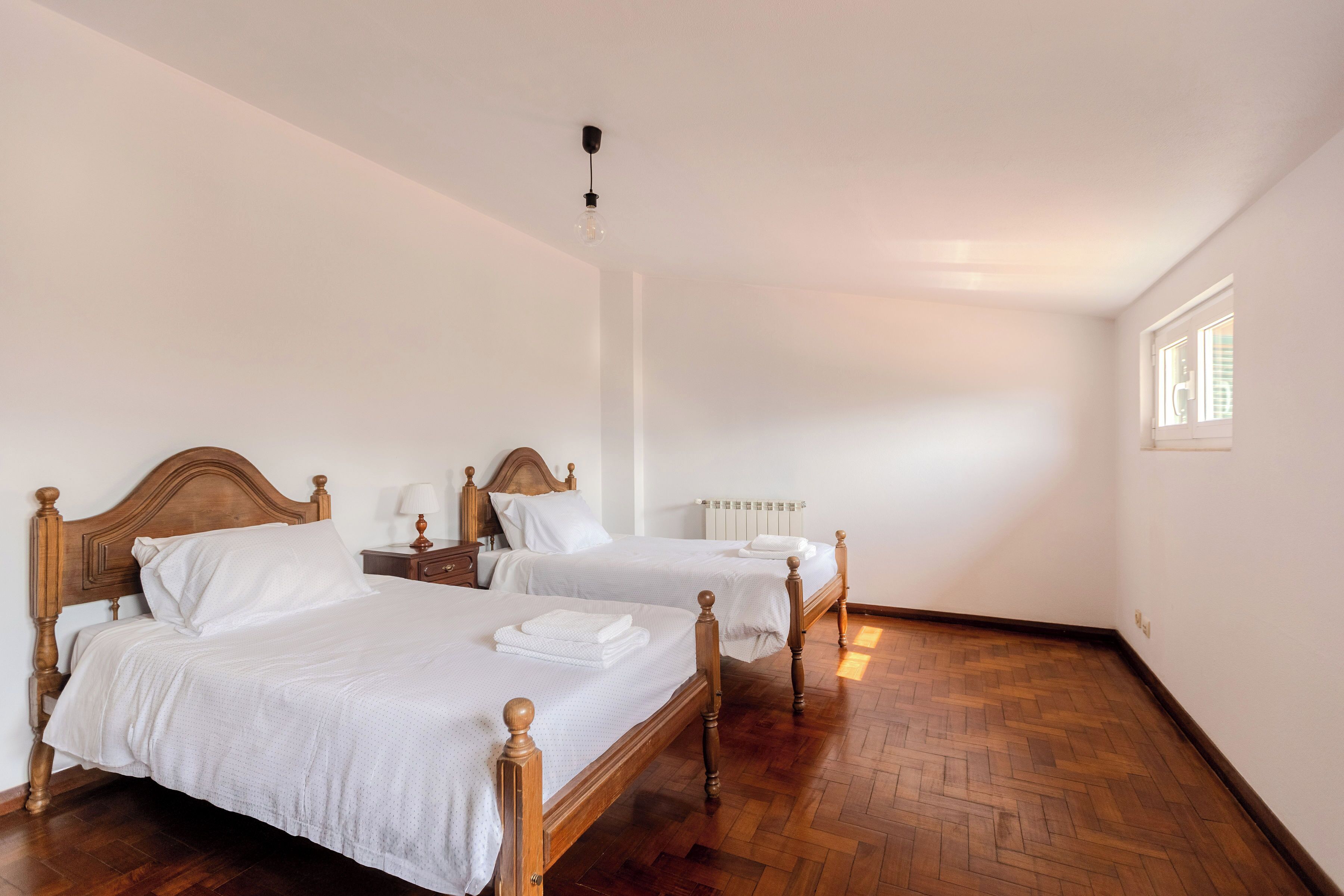 Ein Zimmer mit zwei hölzernen Betten, weißer Bettwäsche, einem Nachttisch aus Holz, einer Lampe und einer Heizung.