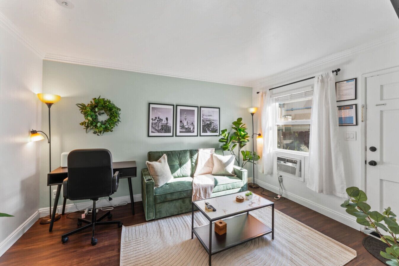 Un salon avec un canapé vert, un fauteuil de bureau noir, une table basse et deux lampes fixées au mur.
