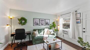 Un salon avec un canapé vert, un fauteuil de bureau noir, une table basse et deux lampes fixées au mur.