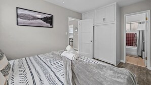 A bedroom with a bed, a ceiling fan, a wardrobe, and a bathroom visible through an open door.