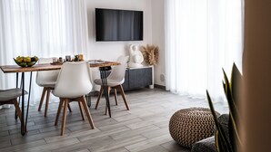 Un comedor moderno con una mesa de madera, sillas blancas y un televisor de pantalla plana montado en la pared.