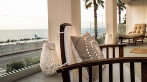 Un balcón con vista al mar, una silla de madera y un banco acolchado.