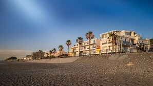 A beachfront hotel with multiple floors, palm trees, and a rocky beach. - Exclusive apartment with sea view, two bedrooms and private parking space (Capo d'Orlando)