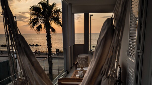 Una hamaca en un balcón con vista a una playa al atardecer.