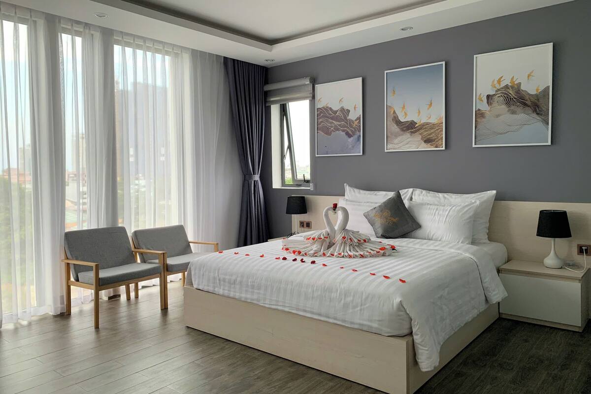 Un dormitorio moderno con una cama grande, dos mesitas de noche, una silla y una obra de arte en la pared.