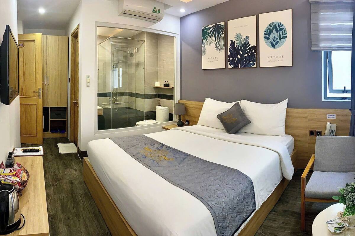 Habitación de hotel con una cama grande, un armario de madera, zona de ducha y un televisor montado en la pared.