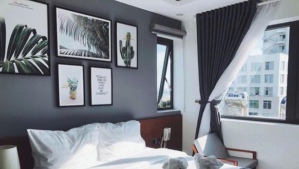 Una habitación de hotel con cama, mesita de noche, lámpara e impresiones enmarcadas de motivos botánicos en la pared.