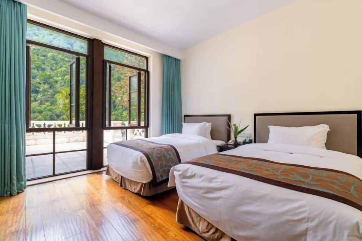 Una camera d'albergo con due letti, un'ampia finestra con tende e un pavimento in legno.