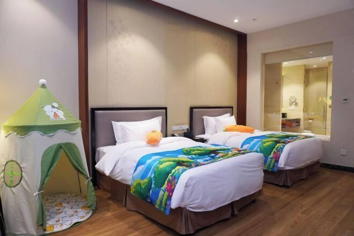 Una camera d'albergo con due letti, una tenda gioco verde e un bagno visibile attraverso una porta aperta.
