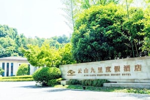 A sign for the Yunnan Nine Cloud Resort Hotel with a clear view of the surrounding greenery and a building in the background. - Nine Cloud Homestead Resort Hotel (Tonglu)