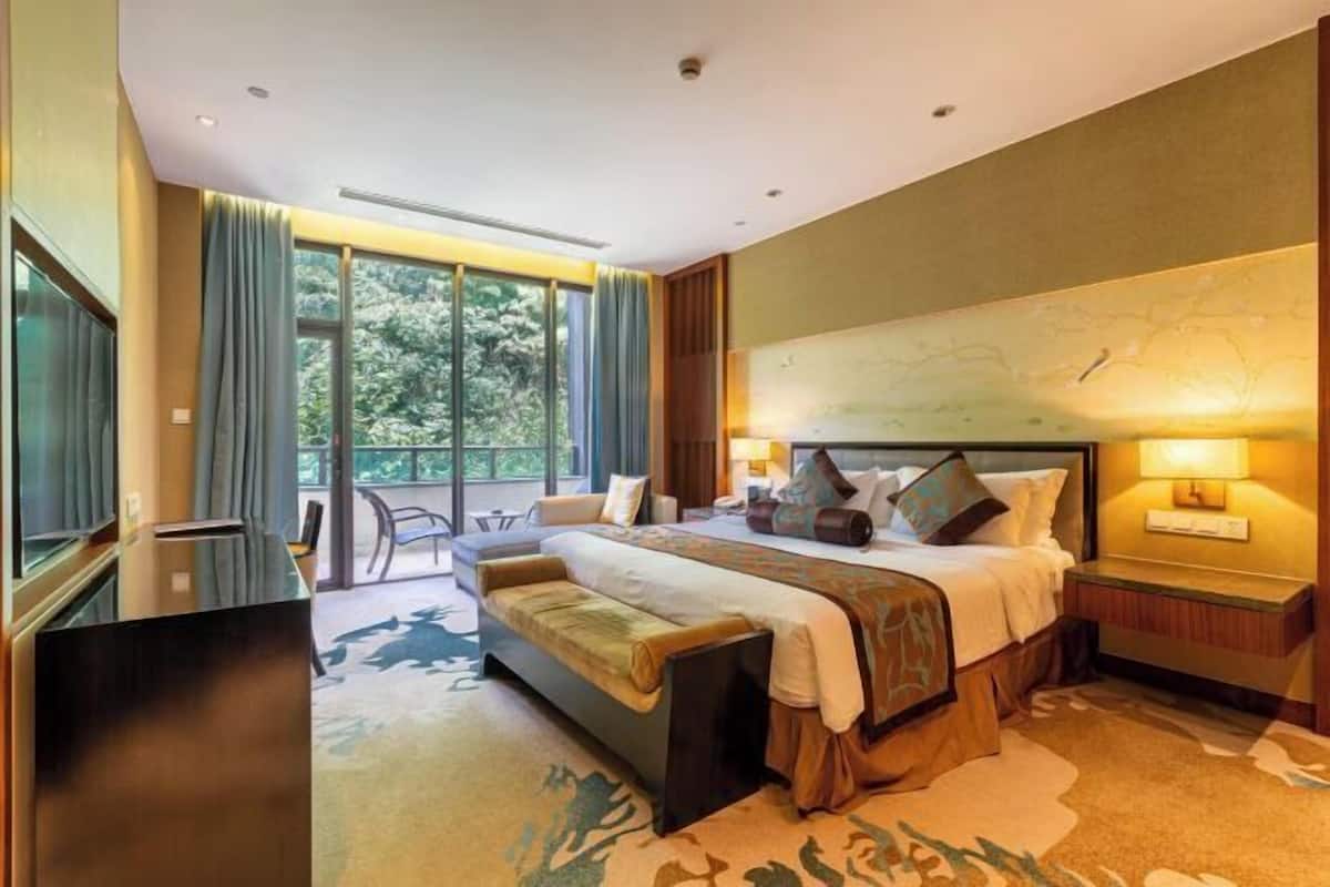 Una camera d'albergo con un letto grande, un divano, una scrivania e vista sul verde dalle finestre.