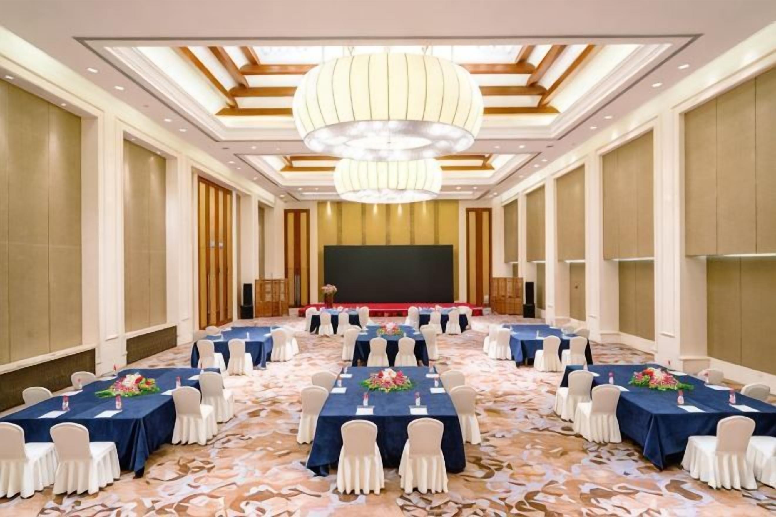 Une salle de conférence équipée de tables et de chaises, d’une scène et d’un grand écran.