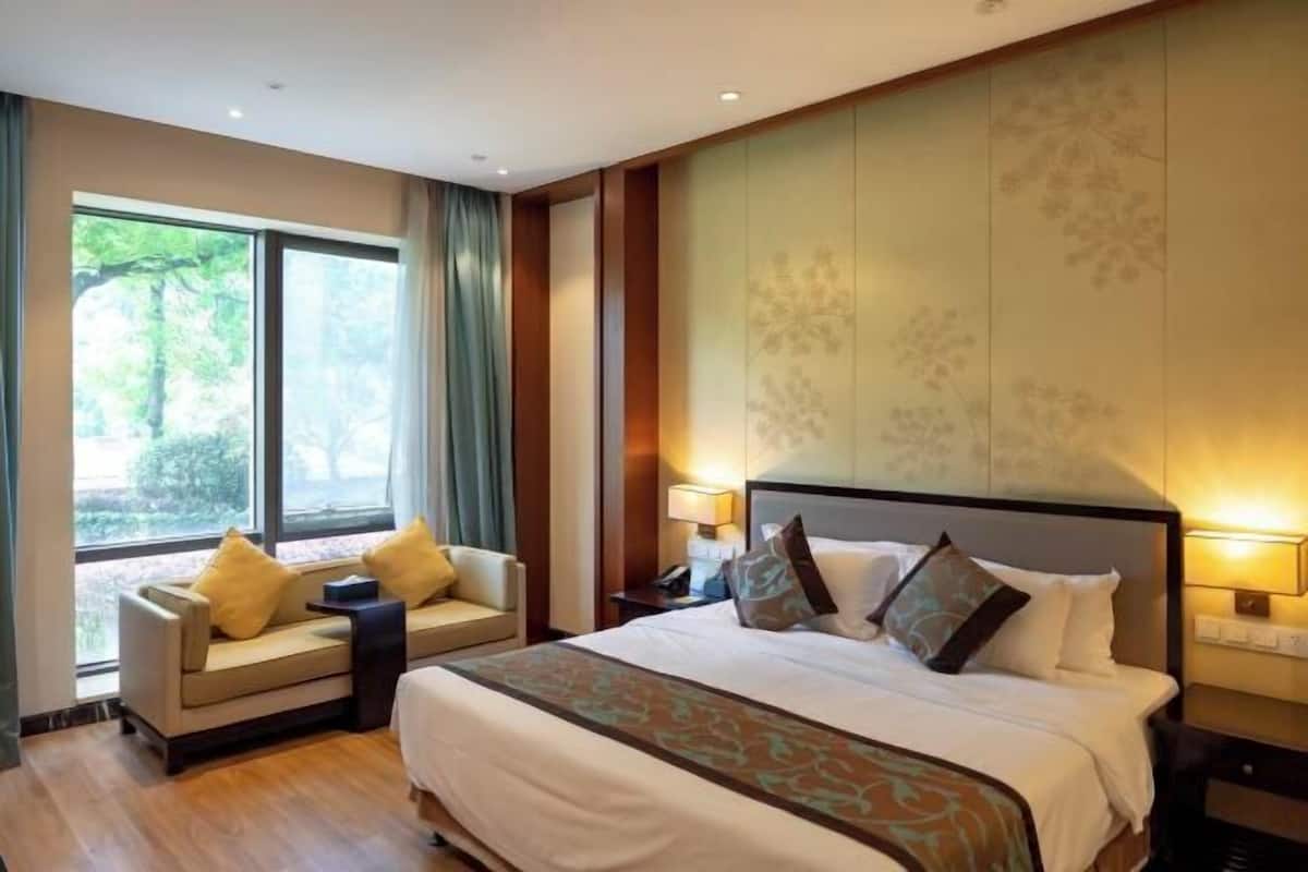 Una camera d'albergo con un letto grande, una poltrona, un comodino e una finestra con tende.
