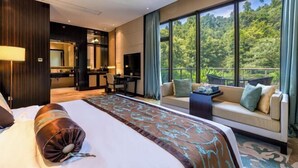 Habitación de hotel moderna con una cama grande, un sofá, un televisor y un balcón con vistas al bosque.