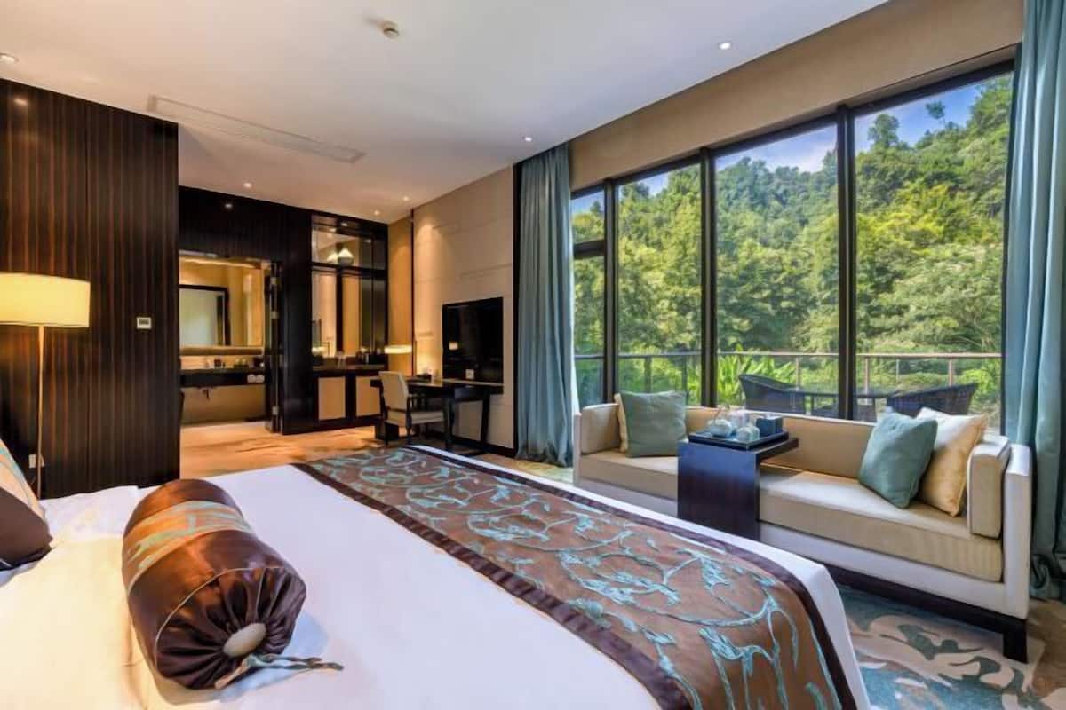 Una moderna camera d'albergo con un letto grande, un divano, una televisione e un balcone vista foresta.