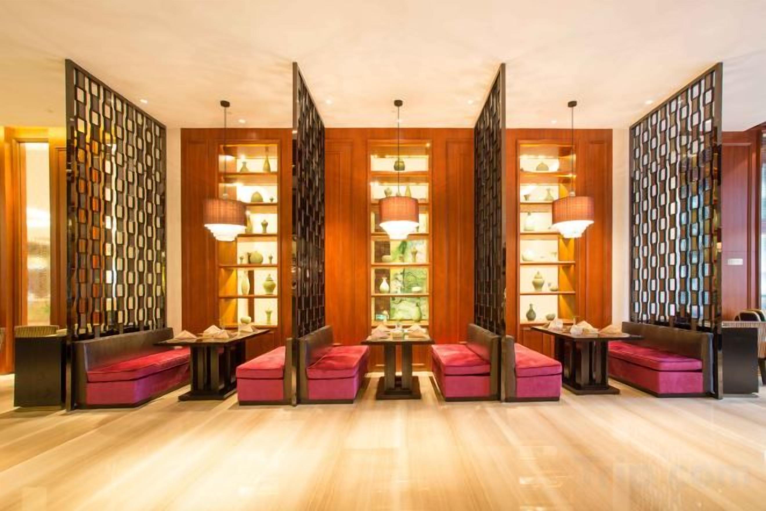A hotel lobby with a central seating area, wooden paneling, and pendant lighting.