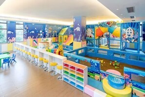 A children's play area with various play structures, a long white table with yellow stools, and a colorful play mat.