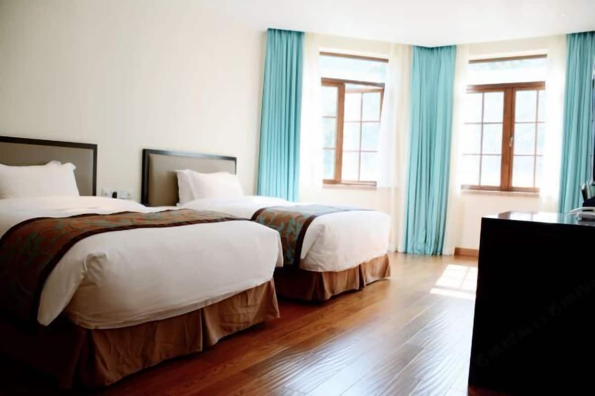 Camera d'albergo con due letti, pavimento in legno e ampie finestre con tende blu.