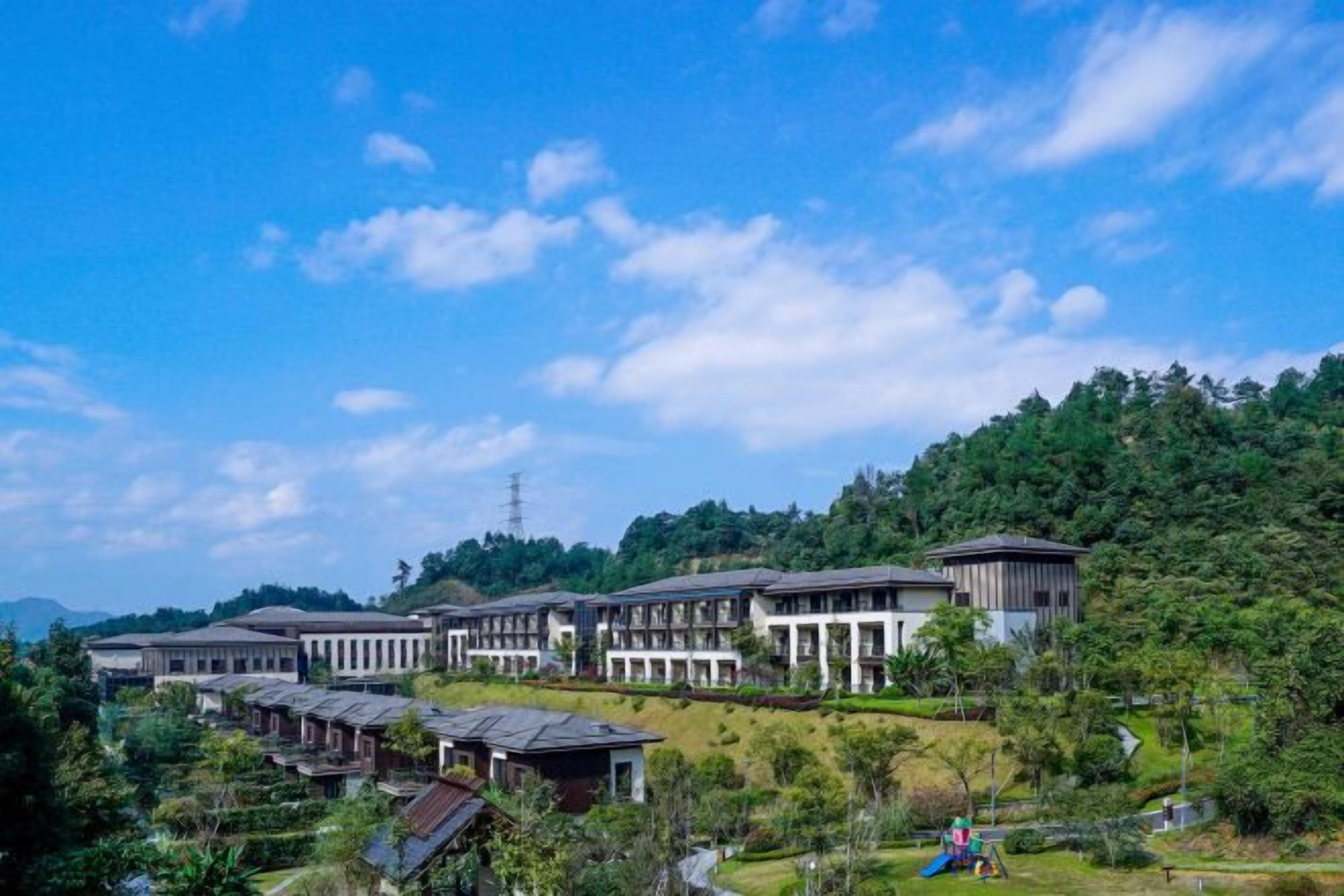 A hotel with multiple buildings, a green landscape, and a clear sky.