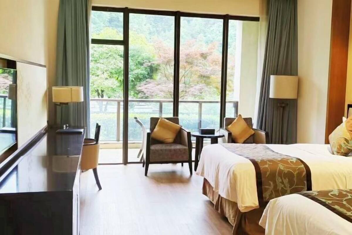Una camera d'albergo con una grande finestra, una scrivania, due sedie e un letto.