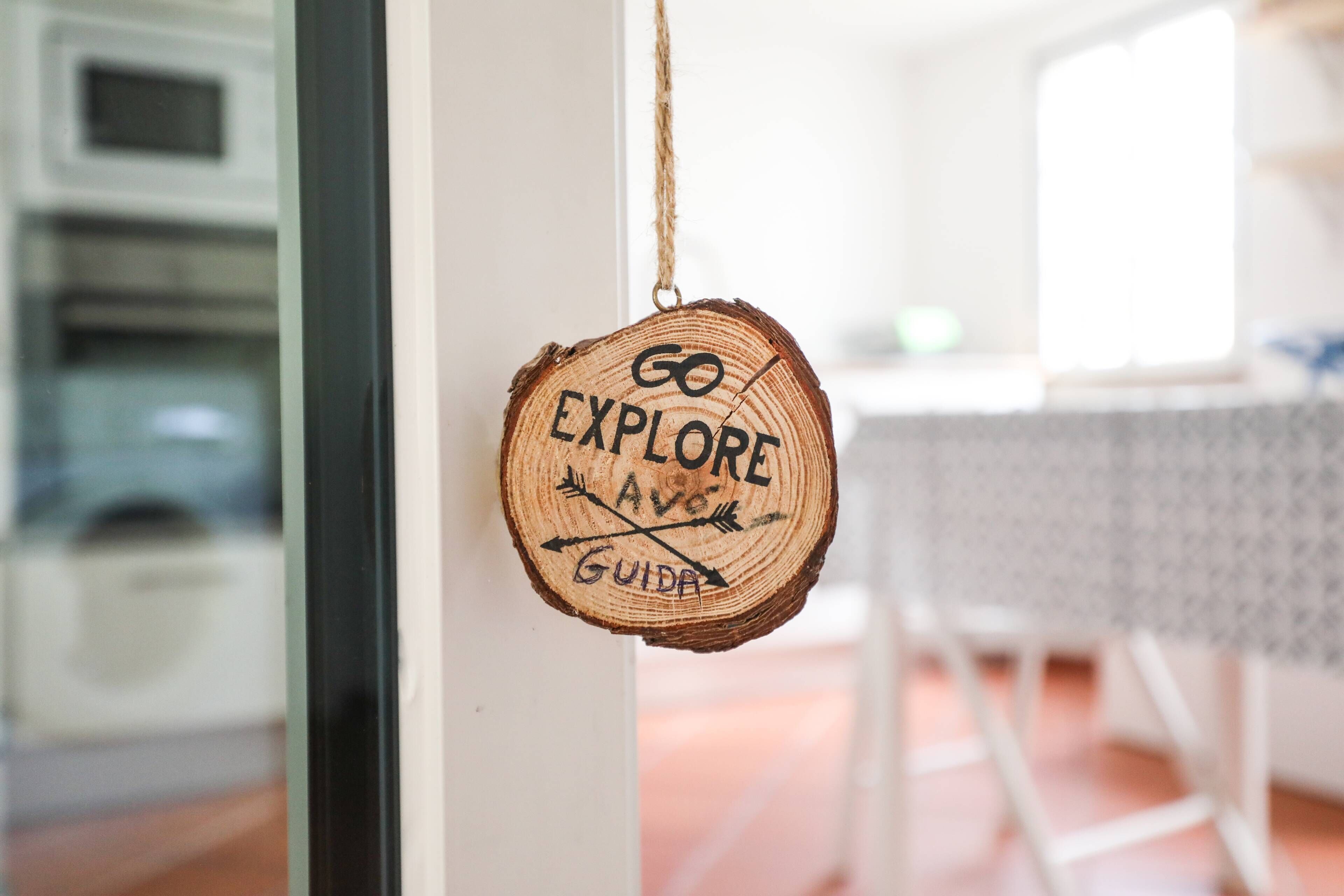 A wooden sign with the words "GO EXPLORE AVE GUIDA" hanging on a door.