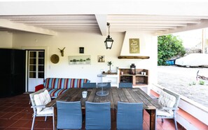 A covered patio with a wooden table and chairs, a striped sofa, and a brick fireplace.