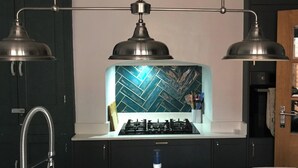 Una cocina con estufa a gas, dos lámparas colgantes y un salpicadero con estampado de espiga.