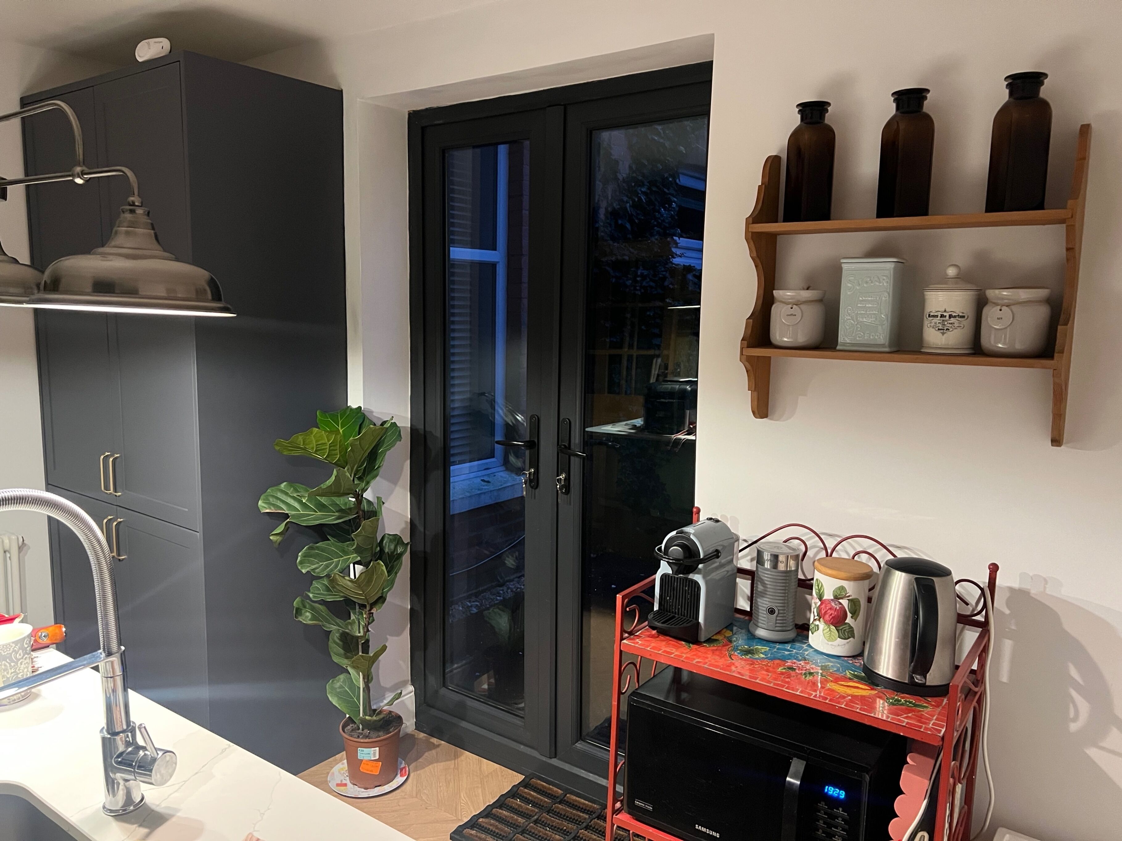 A modern kitchen with a built-in oven, a microwave, and a coffee machine on a red cart.