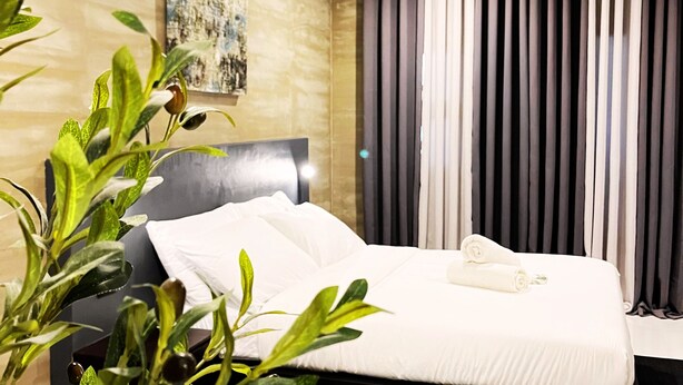 Une chambre d’hôtel moderne, avec un lit, un tableau au mur et une grande fenêtre avec des rideaux.