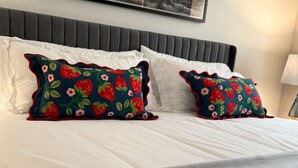 Un lit avec du linge de lit blanc et deux coussins décoratifs à motifs de fraises.