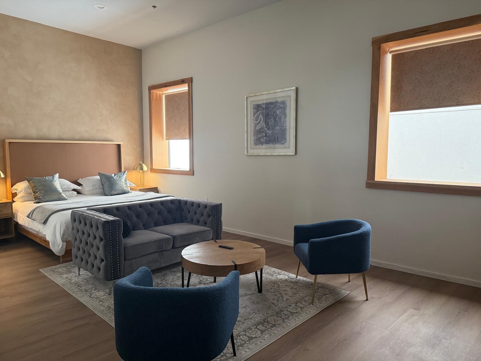 Une chambre à coucher moderne avec un lit, un canapé capitonné, deux fauteuils, une petite table ronde et une grande fenêtre.