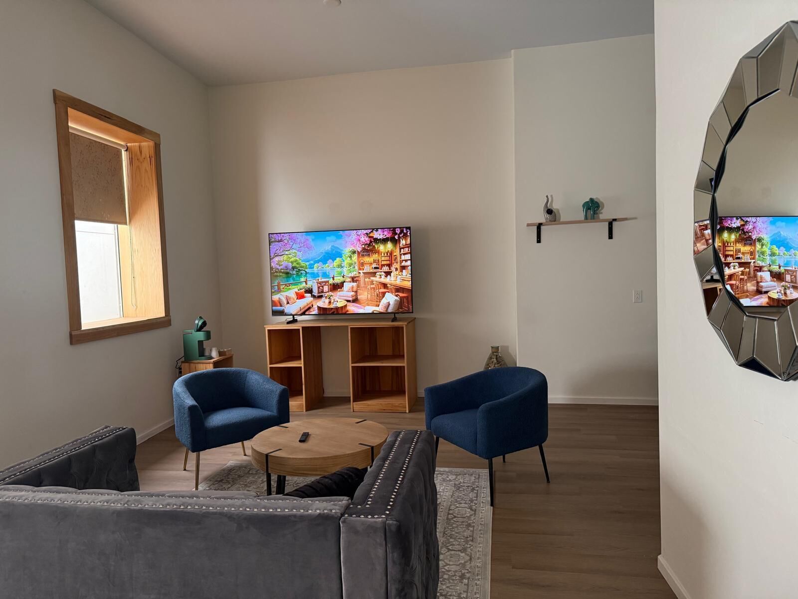 A living room with a TV, two blue chairs, a grey sofa, and a wooden coffee table.