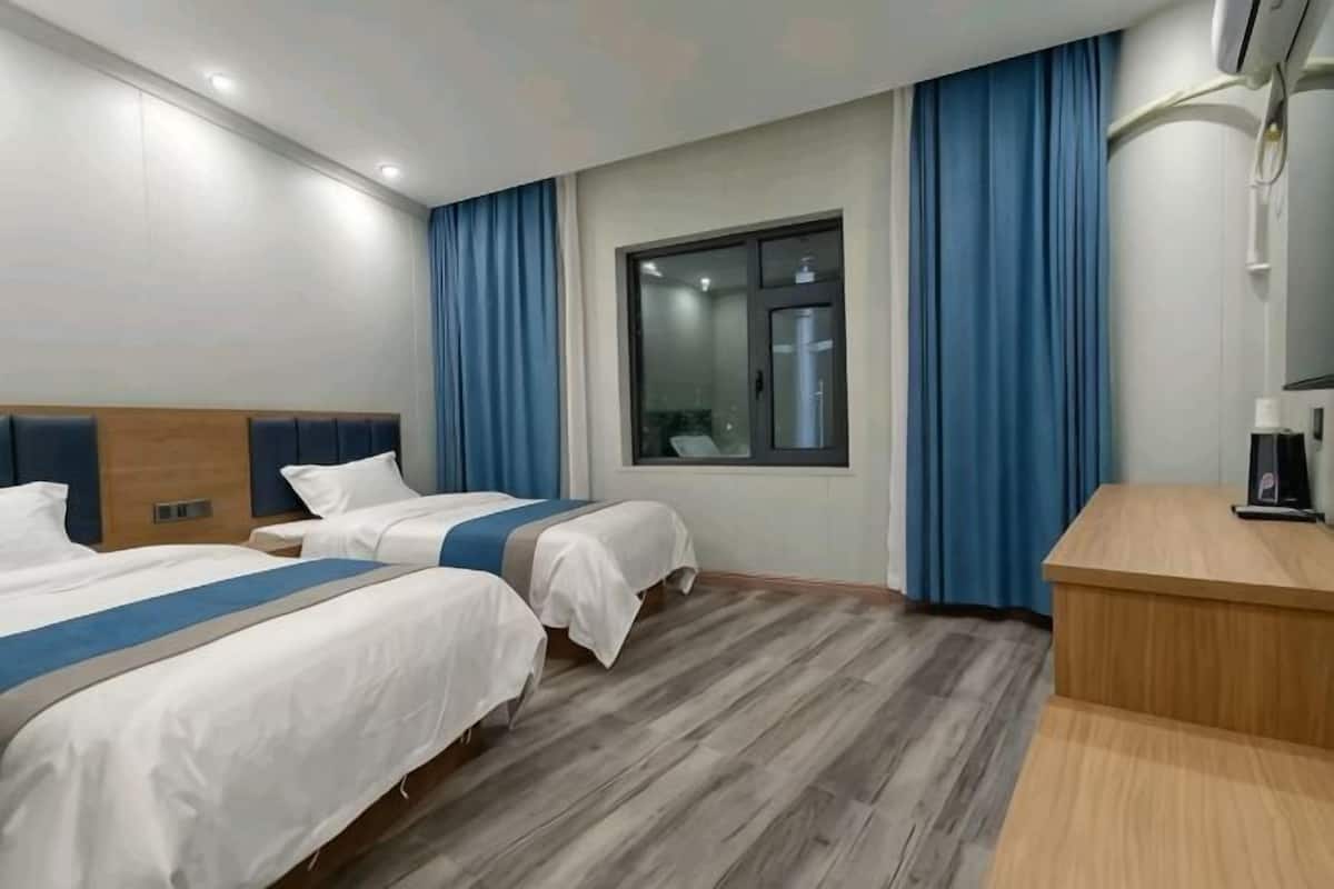 Una camera d'albergo con due letti, una scrivania, una finestra con tende e uno specchio.