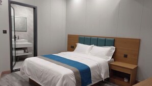 A bedroom with a bed, a nightstand, a wooden headboard, a bathroom with a sink, and a door. - Lanzhou Sapphire Hotel (Lanzhou)