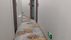 A narrow hallway with patterned carpet, a door at the end, and a green exit sign. - Lanzhou Sapphire Hotel (Lanzhou)