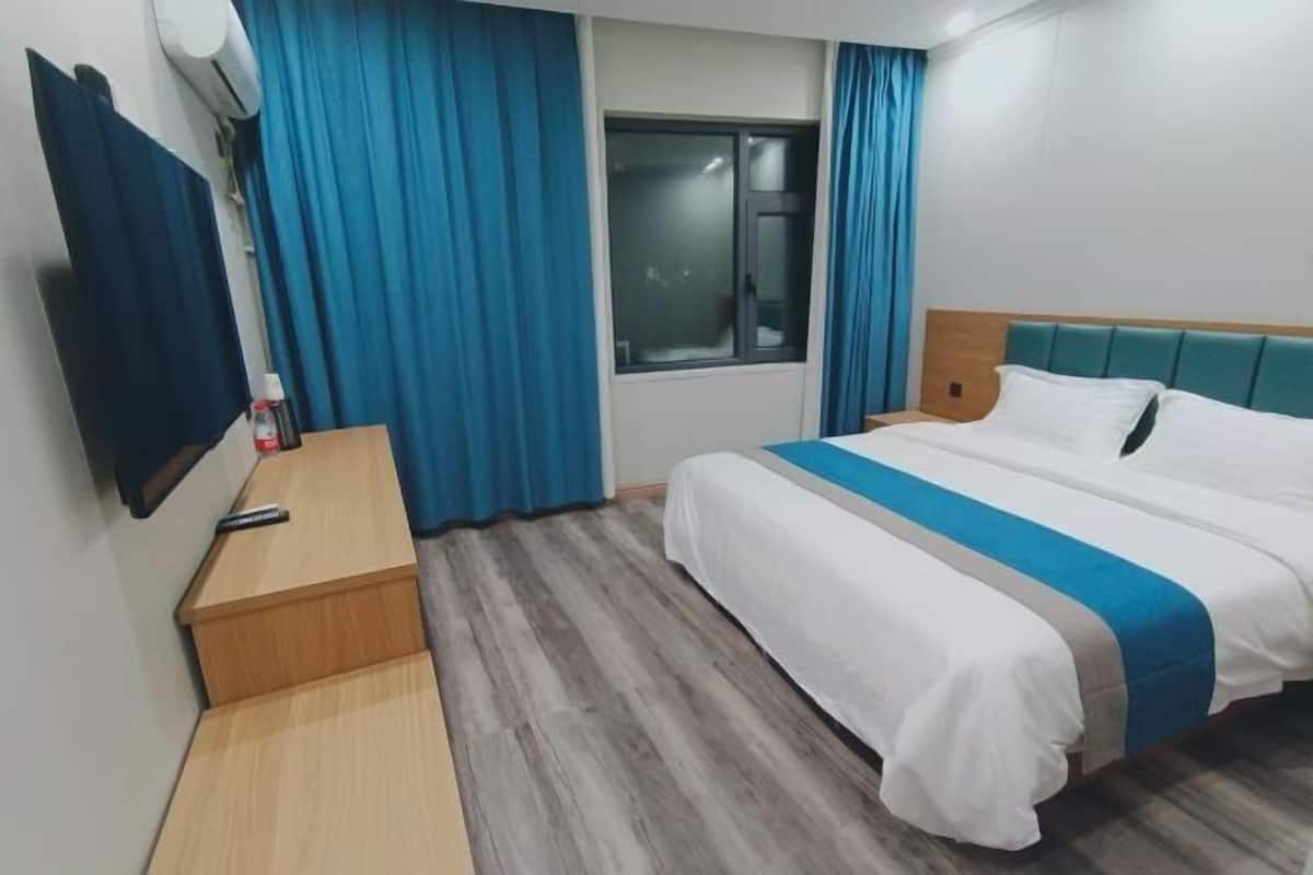 Una camera d'albergo con un letto, un comodino in legno, una televisione e una finestra con tende.