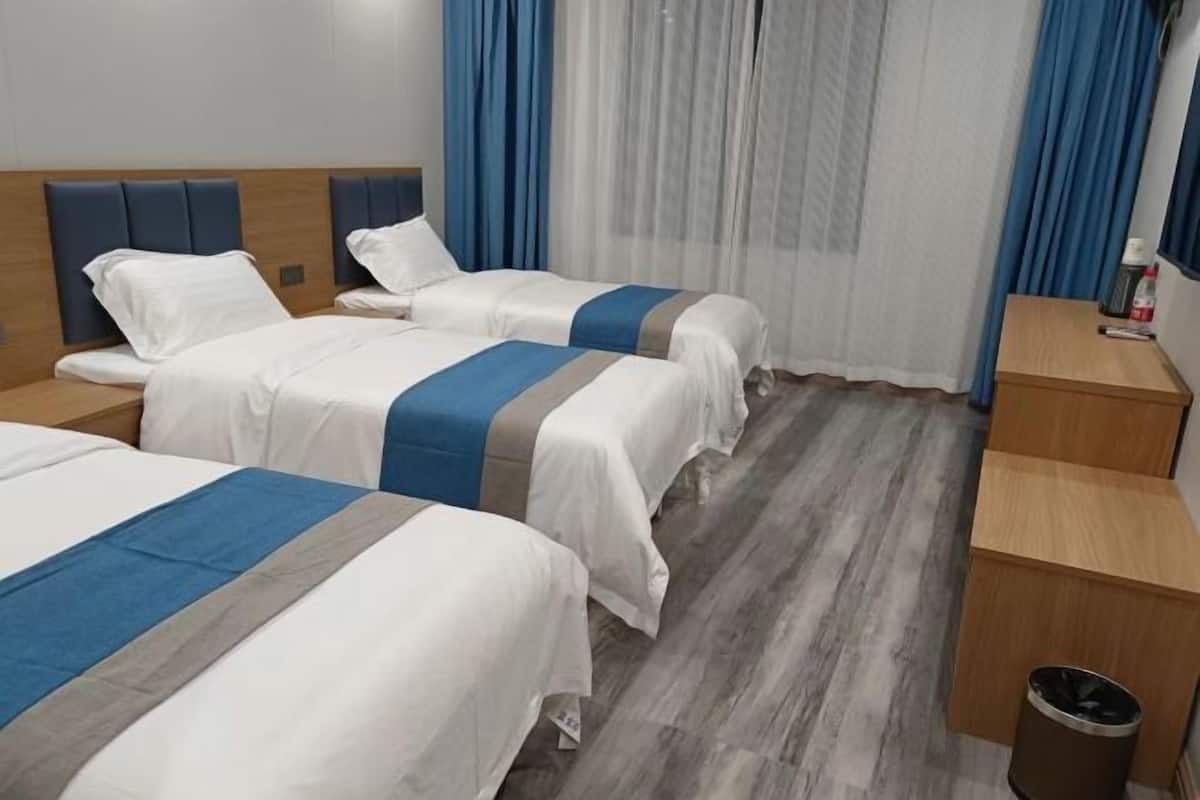 Camera d'albergo con due letti, una testiera in legno, un tavolino, un cestino e una finestra con tende blu.