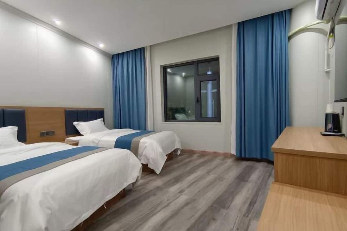 Una camera d'albergo con due letti, una scrivania, una finestra con tende e un pavimento in legno.