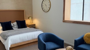 A bedroom with a bed, two blue chairs, a round table, a clock, and a window. - Downtown Boutique Hotel with Popular Cocktail Bar (Tucson)